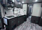 RV kitchen with dark wood cabinets, stainless microwave, and double-basin sink on a granite-style counter.