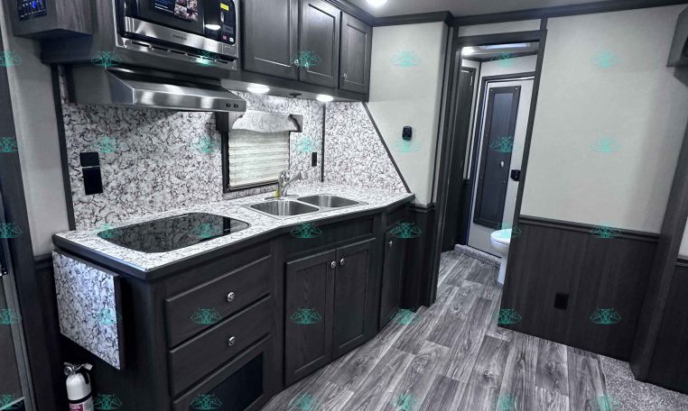 RV kitchen with dark wood cabinets, stainless microwave, and double-basin sink on a granite-style counter.