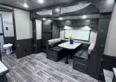 Interior of a dark-wood travel trailer with a booth-style dinette, marble-look table, gray upholstered benches, and overhead cabinets.