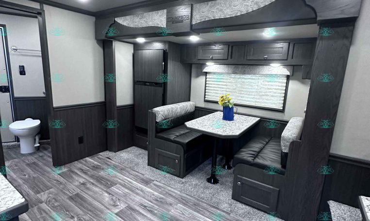 Interior of a dark-wood travel trailer with a booth-style dinette, marble-look table, gray upholstered benches, and overhead cabinets.