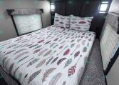 Interior of a trailer bedroom with a large bed and feather-pattern quilt, two pillows, and dark wood cabinetry:**