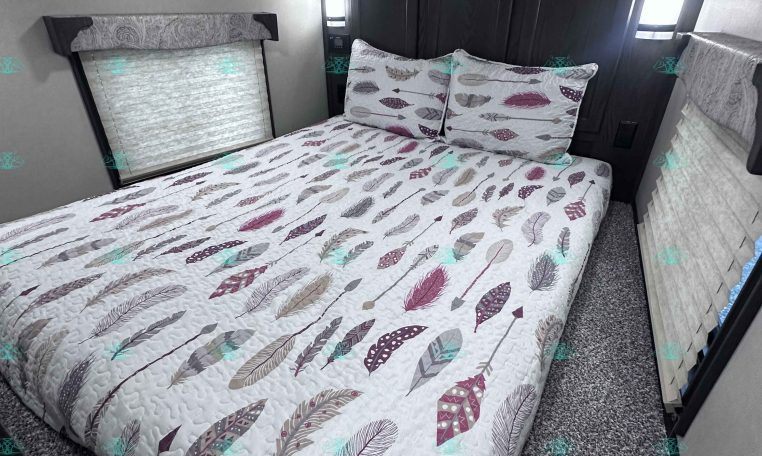 Interior of a trailer bedroom with a large bed and feather-pattern quilt, two pillows, and dark wood cabinetry:**