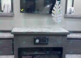 Flat-screen TV mounted on a light-gray wall above a marble-topped cabinet in an RV, with a white decorative leaf sculpture on the right side.