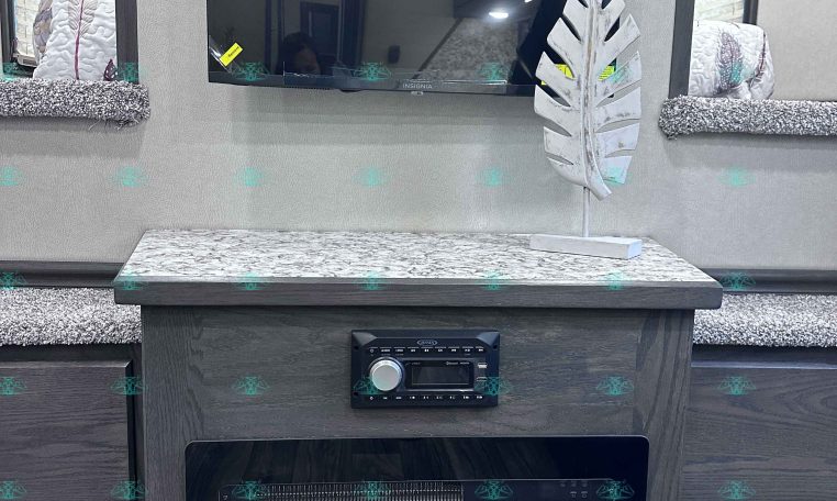 Flat-screen TV mounted on a light-gray wall above a marble-topped cabinet in an RV, with a white decorative leaf sculpture on the right side.