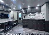 Interior view of a modern RV kitchen with dark wood cabinets, marble countertops, and a central island sink area.