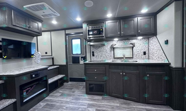 Interior view of a modern RV kitchen with dark wood cabinets, marble countertops, and a central island sink area.