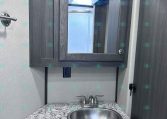 Dark wood bathroom vanity with a framed mirror, granite countertop, and stainless steel faucet fixture.