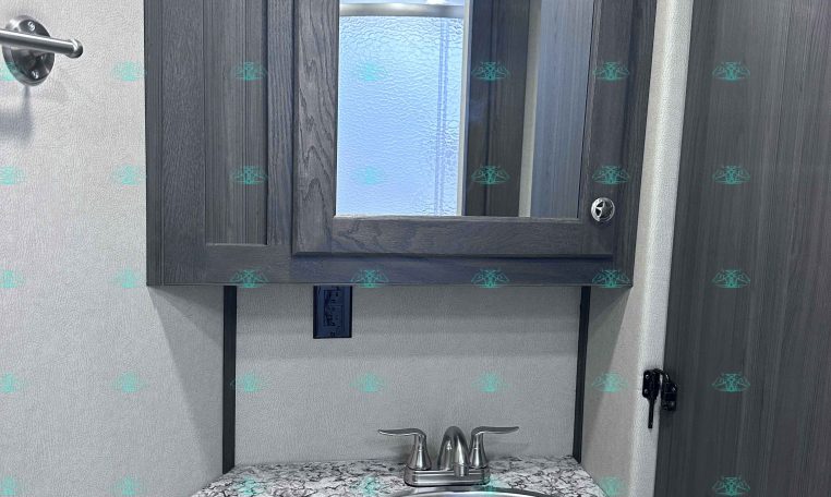 Dark wood bathroom vanity with a framed mirror, granite countertop, and stainless steel faucet fixture.