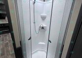 Shower stall with frosted textured glass doors and a handheld shower on a flexible hose inside an RV bathroom.
