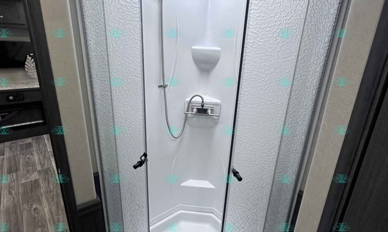 Shower stall with frosted textured glass doors and a handheld shower on a flexible hose inside an RV bathroom.