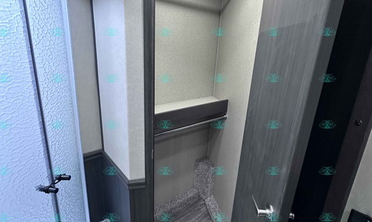 Small RV bathroom with curved glass shower on the left and a dark wood vanity door on the right
