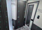 Compact trailer bathroom with a curved glass shower door on the left, dark wood cabinet doors, and a seated toilet on the right.