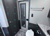 Small trailer bathroom with a toilet, dark wood cabinets, and a granite countertop along the wall
