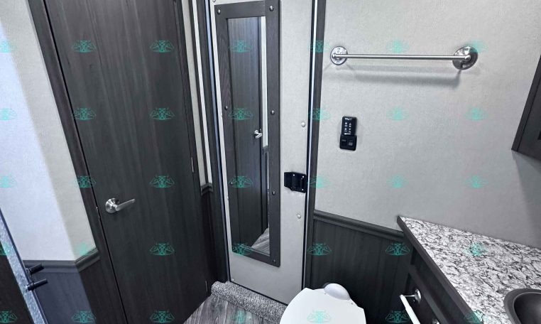 Small trailer bathroom with a toilet, dark wood cabinets, and a granite countertop along the wall