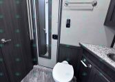 RV bathroom with a white toilet, granite countertop, and dark wood cabinets; a towel bar on the wall and a slim mirror cabinet nearby.