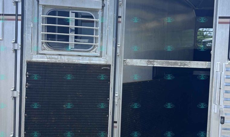 Open trailer door showing interior and a small barred window on the left door; metallic exterior with red/white reflective strip at bottom edge.