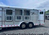 Silver aluminum horse trailer on a gravel lot with open stall doors and windows; another trailer is visible in the background.