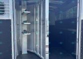 Open livestock trailer with double doors, metal interior, and step shelves on the left; dark empty aisle inside.