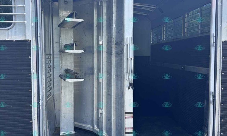 Open livestock trailer with double doors, metal interior, and step shelves on the left; dark empty aisle inside.