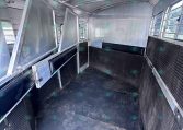 Interior of an empty aluminum horse trailer with divider stalls and a black rubber floor at the rear end of the trailer