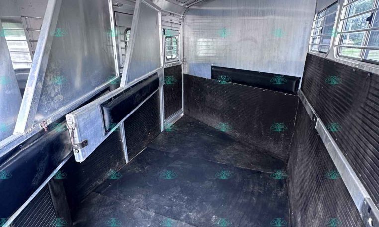 Interior of an empty aluminum horse trailer with divider stalls and a black rubber floor at the rear end of the trailer