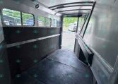 Empty aluminum trailer interior with ribbed walls, windowed side, and open rear door for loading.