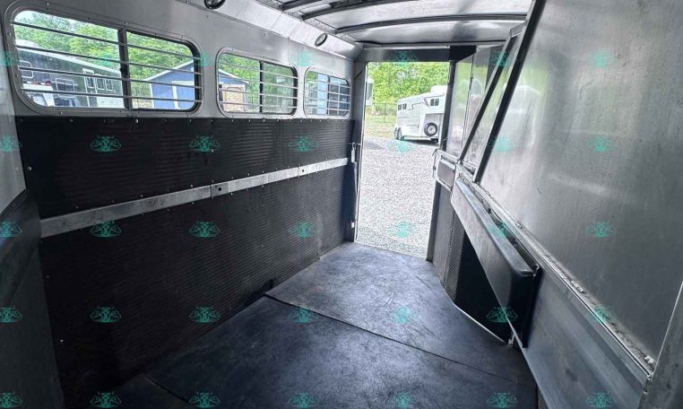 Empty aluminum trailer interior with ribbed walls, windowed side, and open rear door for loading.