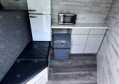 Trailer kitchen: white Galanz refrigerator with top freezer, microwave on a marble countertop, gray cabinets, and a trash can nearby.
