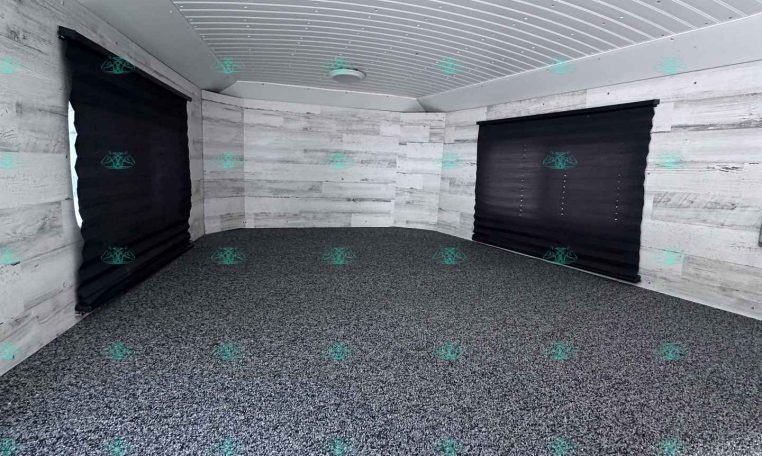 Interior of an empty trailer with a white ribbed ceiling, light gray wood-paneled walls, and two closed black roll-up doors at the ends.