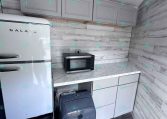 Small kitchen corner with a white retro-style Galanz fridge, gray upper cabinets, microwave on a marble countertop, and a washing machine beneath the counter.