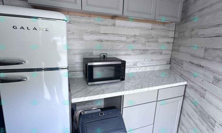 Small kitchen corner with a white retro-style Galanz fridge, gray upper cabinets, microwave on a marble countertop, and a washing machine beneath the counter.