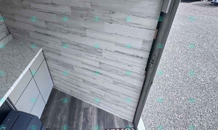 Interior of a small trailer or kitchenette area with gray wood-look walls, a white countertop, and a gray cabinet; a printer sits on the counter near the corner.