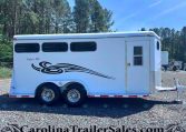 White horse trailer with three small side windows, decorative black swoosh graphics, and a rear door, parked on gravel with a forested backdrop; labeled Classic III.