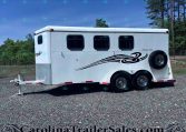 White enclosed horse trailer with three axles and chrome wheels on a gravel lot, trees in the background.