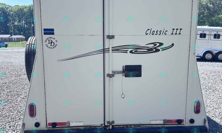 White trailer rear with two vertical doors labeled 'Classic III' and decorative swoosh, parked on gravel with spare tire visible left side.