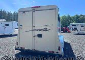 Rear view of a white trailer labeled 'Classic III' with a decorative swoosh, in a gravel RV lot with other trailers and trees in the background.