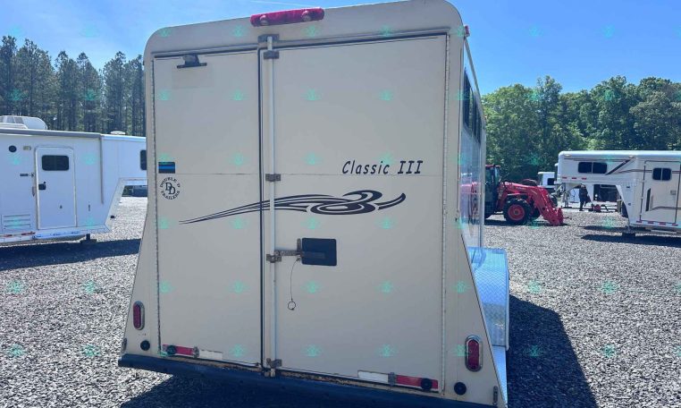 Rear view of a white trailer labeled 'Classic III' with a decorative swoosh, in a gravel RV lot with other trailers and trees in the background.