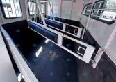 Interior of a horse trailer with dividing metal stalls and dark rubber-matted floor