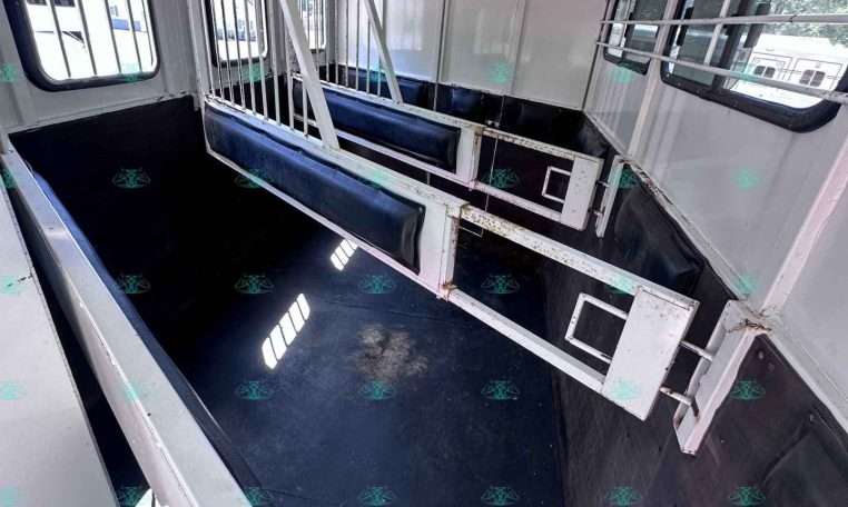 Interior of a horse trailer with dividing metal stalls and dark rubber-matted floor