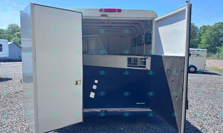Open horse trailer with interior stall and partition, parked on gravel lot