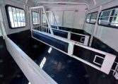 Interior of a white livestock trailer with metal stalls, blue padded benches, and barred side windows.