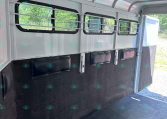 Interior of a white horse trailer with barred windows and dark padded walls, ready for loading horses or gear