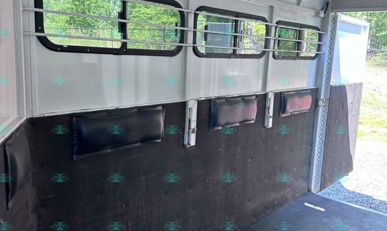 Interior of a white horse trailer with barred windows and dark padded walls, ready for loading horses or gear
