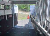 Interior of an empty horse trailer with stall dividers and rubber floor, open rear door to outdoors.