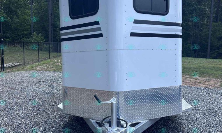 Front view of a white enclosed trailer with two windows and black stripe decals, parked on gravel. Maintains hitch and diamond-plate base visible at the bottom.
