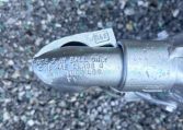 Close-up of a metal trailer hitch coupler with stamped text on a gravel surface, showing specifications and a worn, damp finish.