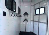 Interior of a white utility trailer with black hooks along the left wall, side windows, and a textured rubber floor.