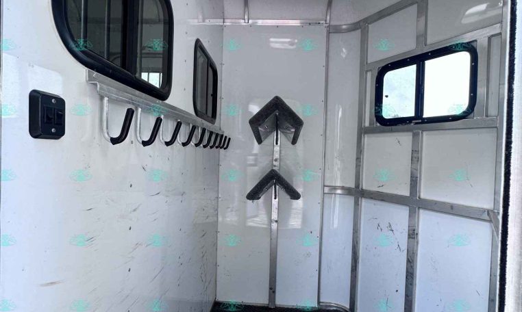 Interior of a white utility trailer with black hooks along the left wall, side windows, and a textured rubber floor.