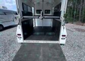 Open horse trailer with ramp down, showing divider stalls and padded walls inside. (informative)