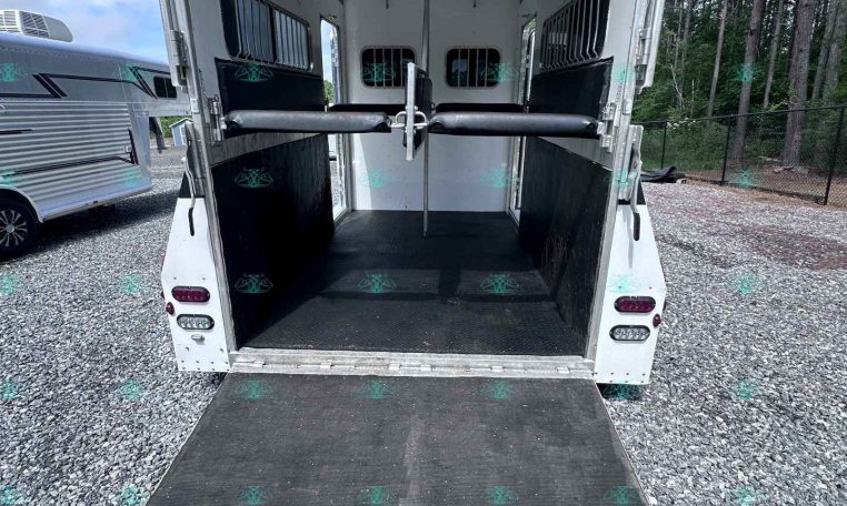Open horse trailer with ramp down, showing divider stalls and padded walls inside. (informative)